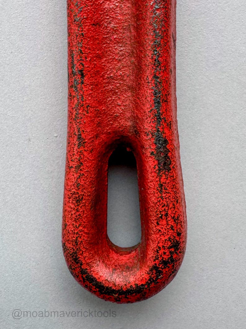 May include: Close-up of a red metal tool with a textured surface and a loop at the end. The red paint is chipped, revealing black underneath. The text "@moabmavericktools" is at the bottom.