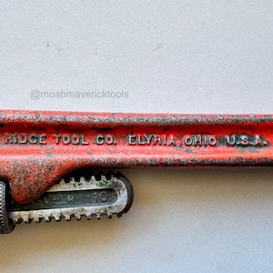 May include: A vintage red and silver pipe wrench with the text "THE RIDGE TOOL CO. ELYRIA, OHIO U.S.A. 10". The wrench is 10 inches long and shows signs of wear.