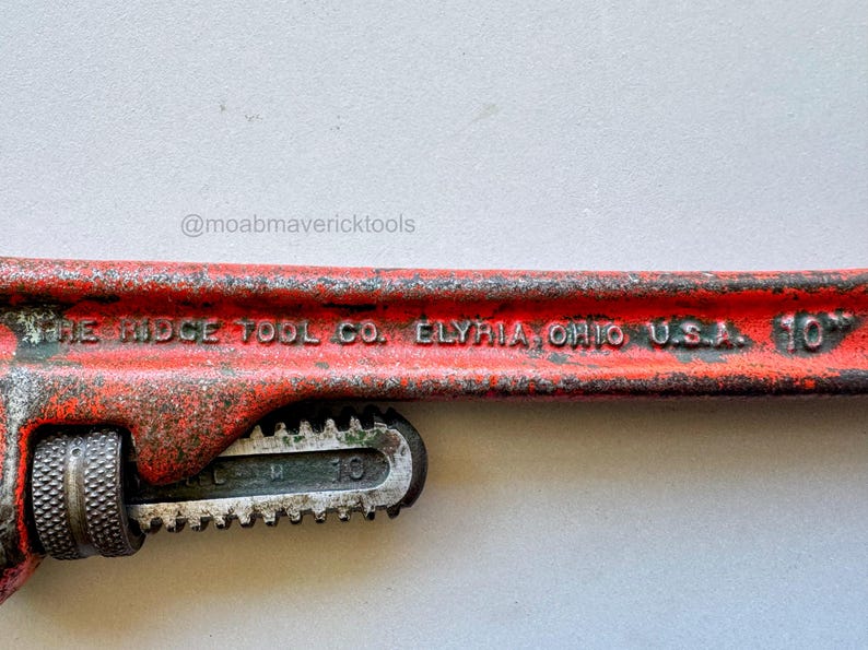 May include: A vintage red and silver pipe wrench with the text "THE RIDGE TOOL CO. ELYRIA, OHIO U.S.A. 10". The wrench is 10 inches long and shows signs of wear.