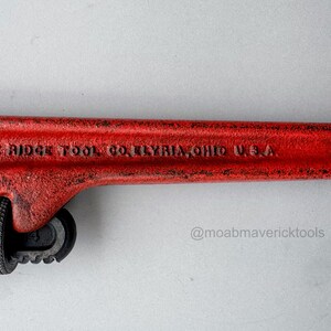 May include: A red 14-inch pipe wrench with the text "THE RIDGE TOOL CO. ELYRIA, OHIO U.S.A." is displayed against a white background. The wrench has a black adjustable jaw and a textured handle.