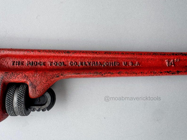 May include: A red 14-inch pipe wrench with the text "THE RIDGE TOOL CO. ELYRIA, OHIO U.S.A." is displayed against a white background. The wrench has a black adjustable jaw and a textured handle.