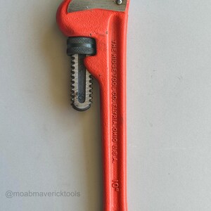 May include: A bright red 10-inch pipe wrench with a black jaw and handle. The wrench has the text "THE RIDGE TOOL CO. ELYRIA, OHIO U.S.A." printed on the handle. The wrench is designed for gripping and turning pipes.