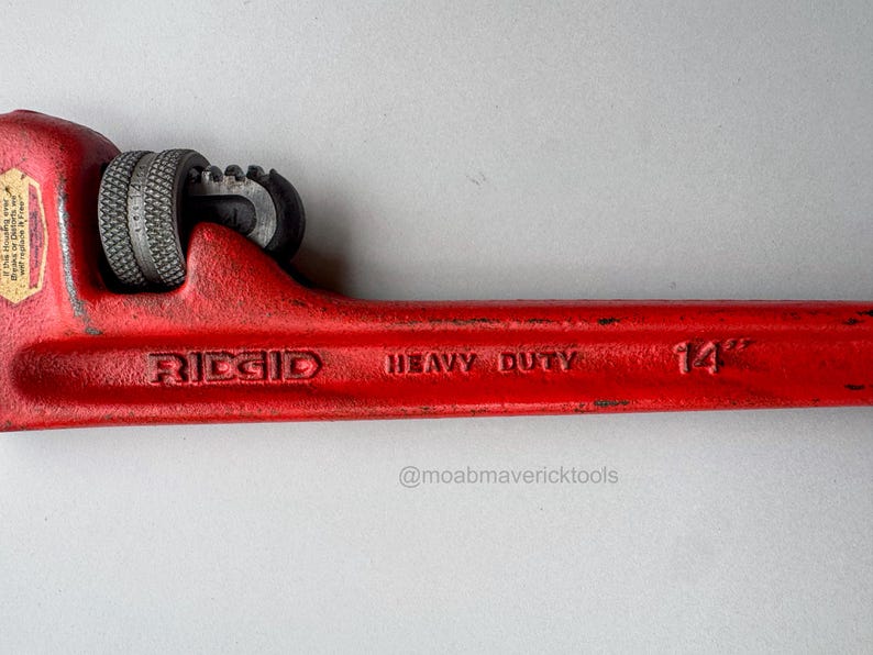 May include: A red Ridgid heavy-duty pipe wrench. The wrench is 14 inches long and features a textured grip and adjustable jaws. The tool is designed for heavy-duty use and is a vibrant red color.