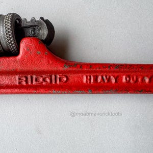 May include: Close-up of a red RIDGID HEAVY DUTY pipe wrench. The wrench has a textured grip and adjustable jaws. The text "RIDGID HEAVY DUTY" is embossed on the handle. The wrench is a tool for plumbing and construction.