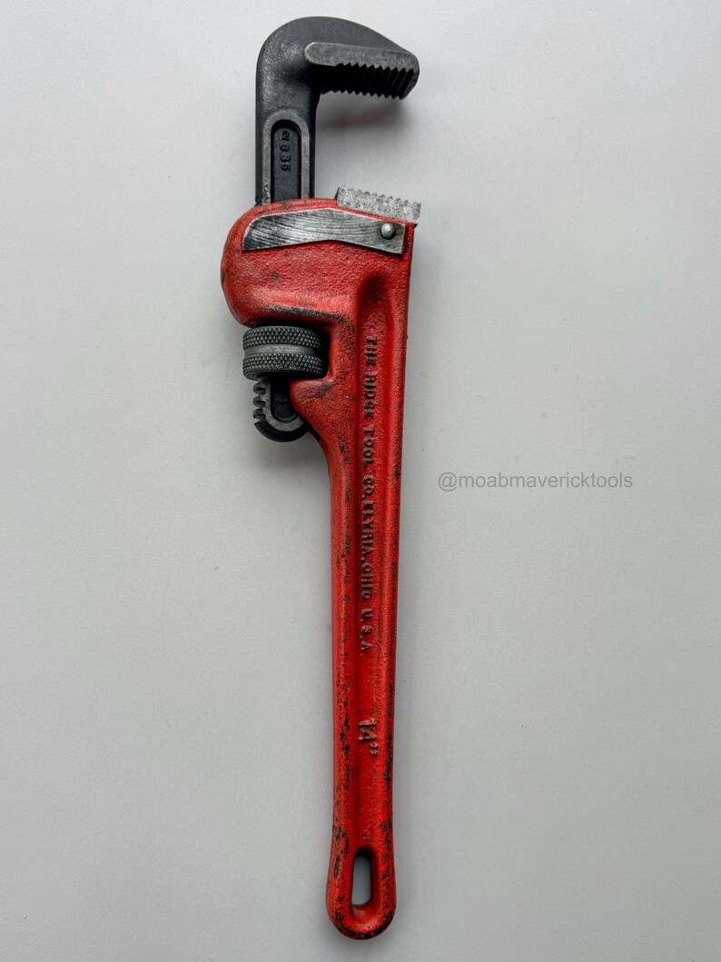 May include: A red and black pipe wrench, 14 inches long, with a toothed jaw. The wrench has the text "THE RIDGE TOOL CO. ELYRIA, OHIO U.S.A." and the Instagram handle "@moabmavericktools" printed on it.