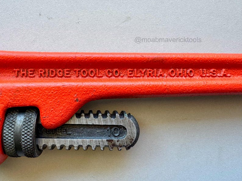 May include: Close-up of a red pipe wrench with the text "THE RIDGE TOOL CO. ELYRIA, OHIO U.S.A." The wrench has a black adjustable jaw and a textured handle. The number "10" is visible on the jaw.