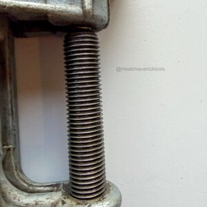May include: Close-up of a vintage metal clamp with a threaded rod. The clamp is a dull silver color, showing signs of wear. The rod is tightly threaded, suggesting it's designed for securing objects. The image includes the text "@moabmavericktools".