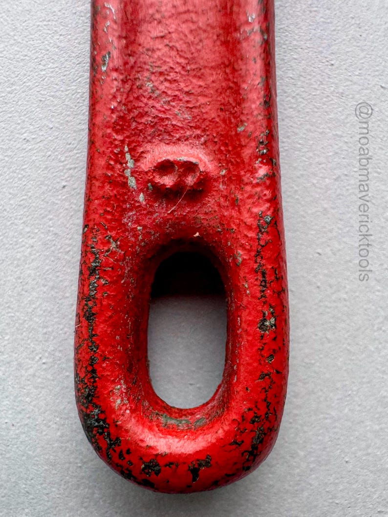 May include: Close-up of a red metal tool with a large oval opening. The tool has a textured, worn appearance with black markings, suggesting age and use. The red paint shows signs of wear.