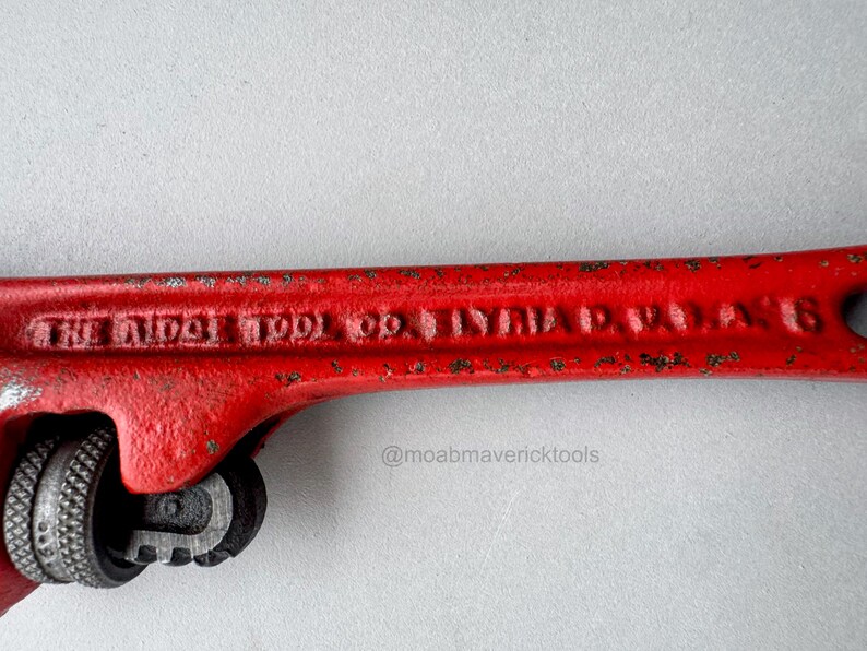May include: Close-up of a vintage red pipe wrench. The wrench has the text "THE RIDGE TOOL CO. ELYRIA O. U.S.A. 6" embossed on the handle. The wrench is a classic tool.
