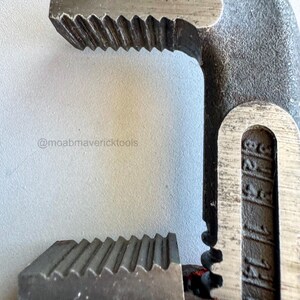 May include: Close-up of a heavy-duty pipe wrench. The wrench is made of dark gray metal with a red handle. The jaws have sharp, angled teeth for gripping pipes. The text "@moabmavericktools" is visible.