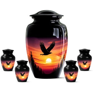 May include: A large black cremation urn centered among four smaller matching urns. Each vessel features a glossy finish with a vibrant sunset scene depicting a soaring eagle, silhouetted pine trees, and a bright sun against an orange sky.