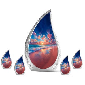 May include: A large teardrop-shaped cremation urn and four smaller matching keepsake urns. Each vessel features a silver metallic frame with intricate etched patterns and a central glossy panel depicting a vibrant sunset over an ocean beach.