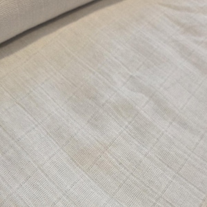 May include: A roll of off-white, textured fabric with a grid-like pattern. The fabric appears to be lightweight and possibly linen or cotton. The material is folded over itself, showing the texture and weave of the cloth.