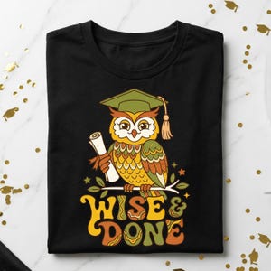 May include: Black t-shirt featuring a colorful owl wearing a graduation cap and holding a diploma. The owl is perched on a branch with the words "WISE & DONE" in a retro font. A graduation-themed graphic tee.