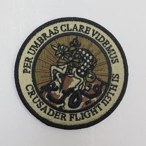 Può includere: Toppa rotonda ricamata con la scritta "PER UMBRAS CLARE VIDEMUS" e "CRUSADER FLIGHT 113TH IS". La toppa presenta un'illustrazione dettagliata di un cavaliere a cavallo, con un motivo a scacchi.