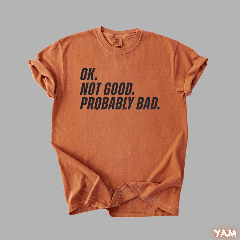 Pu&ograve; includere: T-shirt arancione bruciato con la scritta "OK. NOT GOOD. PROBABLY BAD." in nero. La maglietta &egrave; piegata e ha le maniche arrotolate. La maglietta &egrave; realizzata in un materiale morbido, probabilmente cotone.