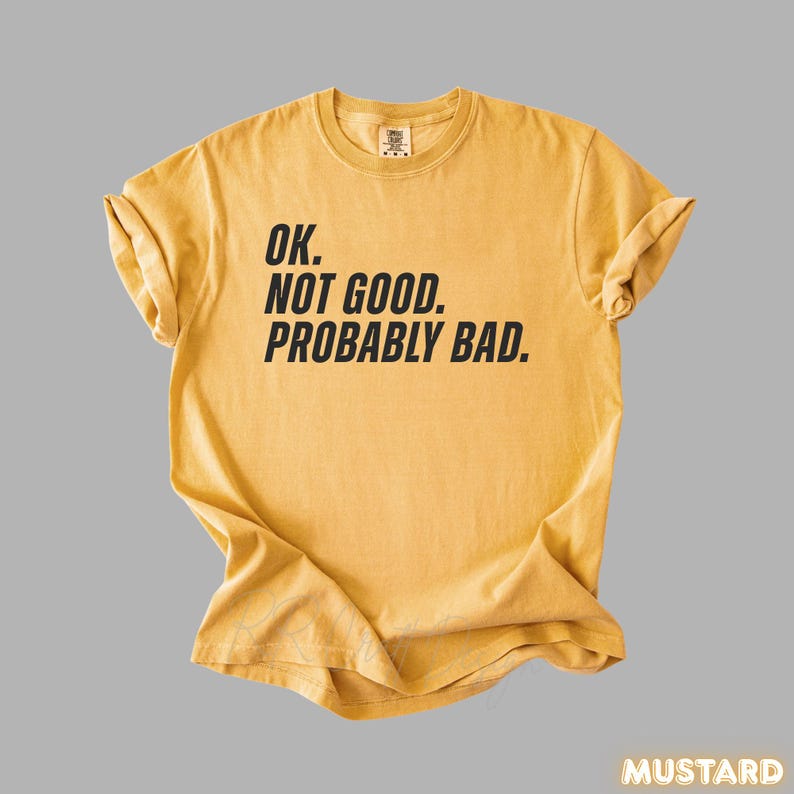 Pu&ograve; includere: T-shirt color senape con la scritta "OK. NOT GOOD. PROBABLY BAD." in nero. La maglietta &egrave; a girocollo e ha le maniche arrotolate. La parola "MUSTARD" &egrave; in basso a destra.