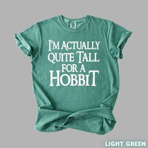 Puede incluir: Camiseta verde claro con el texto blanco "I'm Actually Quite Tall For A Hobbit". La camiseta es de cuello redondo con mangas enrolladas. La esquina inferior derecha de la camiseta tiene las palabras "Light Green".