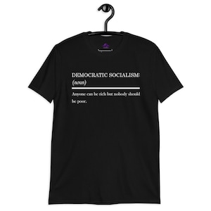 May include: A black short-sleeved t-shirt featuring white text that reads: DEMOCRATIC SOCIALISM: (noun) Anyone can be rich but nobody should be poor. The shirt is displayed on a black hanger against a plain background, showcasing the graphic design.