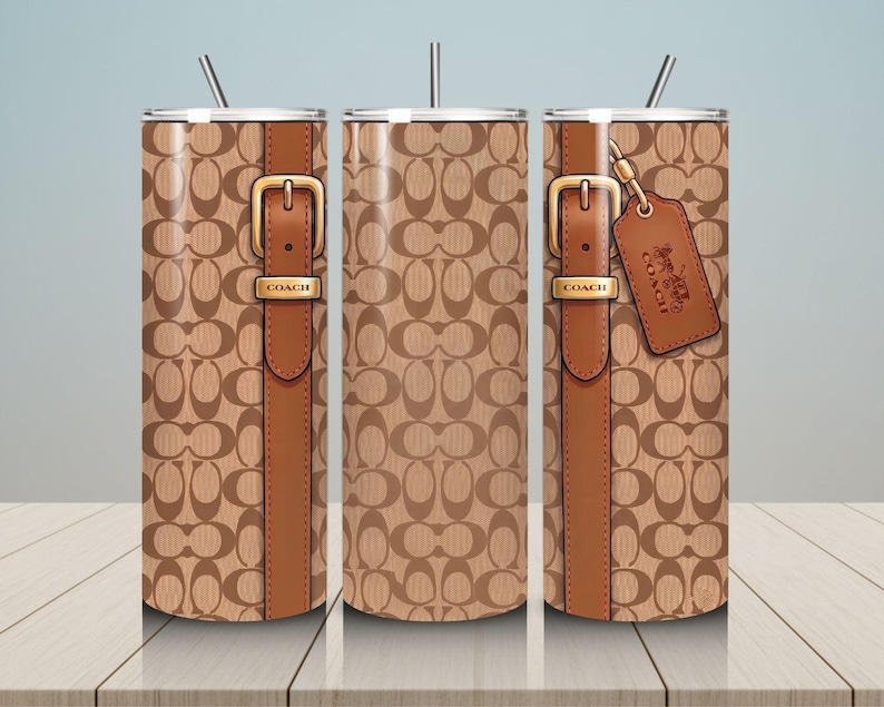 May include: A cylindrical tumbler with a straw, featuring a tan and brown repeating logo pattern. The design includes a vertical brown strap graphic with a gold-toned buckle labeled COACH and a hanging brown leather-style luggage tag with a logo.