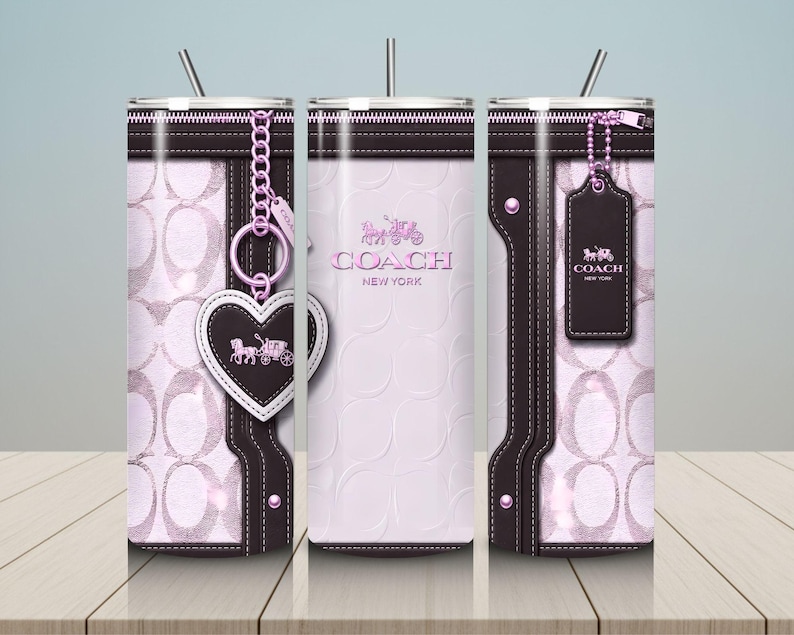 May include: A cylindrical tumbler featuring a light pink and dark brown design with a repeating logo pattern. The exterior displays a zipper graphic, a heart-shaped charm, and a rectangular luggage tag, all printed with the Coach New York logo.