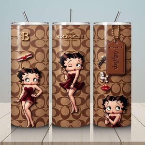May include: A set of three stainless steel tumblers featuring a brown Coach pattern with Betty Boop illustrations. Each tumbler has a different design, including a gold letter "B", a Coach tag, and various Betty Boop themed charms. The tumblers have silver straws.