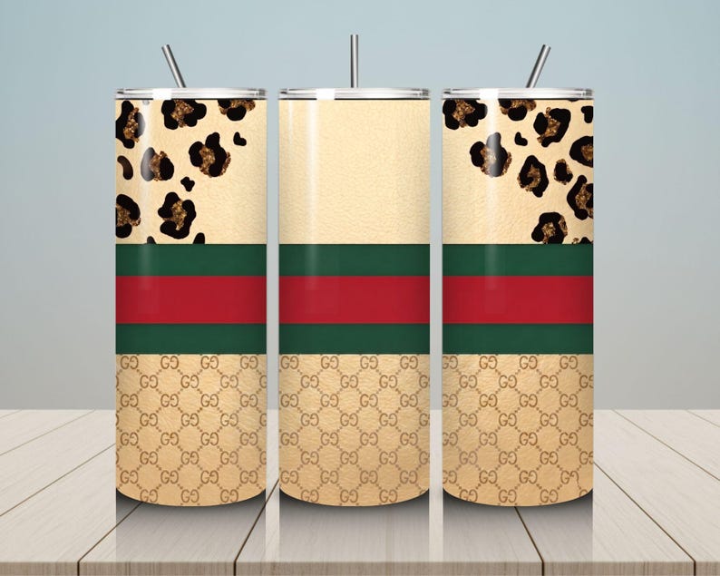 May include: Three cylindrical tumblers with lids and straws. The design features a top section with a black and gold leopard print, a middle section with a horizontal red stripe bordered by two green stripes, and a bottom section with a gold monogram pattern.