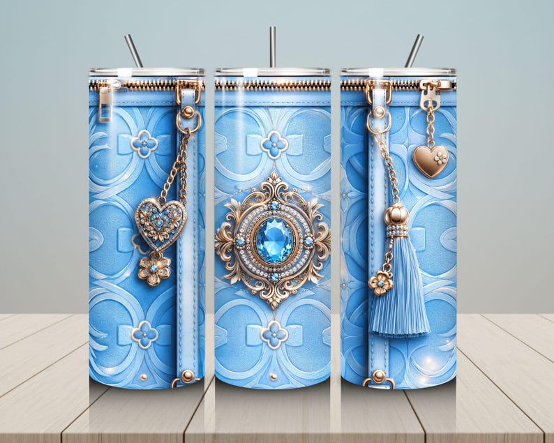 May include: A light blue tumbler with a decorative design. The tumbler features a zipper top, a heart-shaped charm, and a tassel. The design includes a floral pattern and a large, ornate jewel in the center. A straw is inserted in the lid.