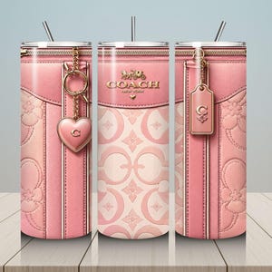 May include: Pink Coach-branded tumbler with a zipper design, gold accents, and a heart-shaped charm. The tumbler features a light pink floral pattern and a tag with the Coach logo. Includes a silver straw.