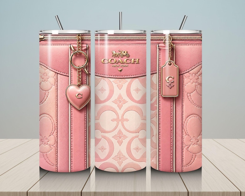 May include: Pink Coach-branded tumbler with a zipper design, gold accents, and a heart-shaped charm. The tumbler features a light pink floral pattern and a tag with the Coach logo. Includes a silver straw.