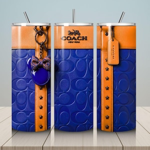 May include: Three cylindrical tumblers with straws featuring a blue embossed logo pattern, a tan leather-look band, and star studs. One tumbler displays a Coach logo, another a hanging bow charm, and the third a hanging leather-look luggage tag.