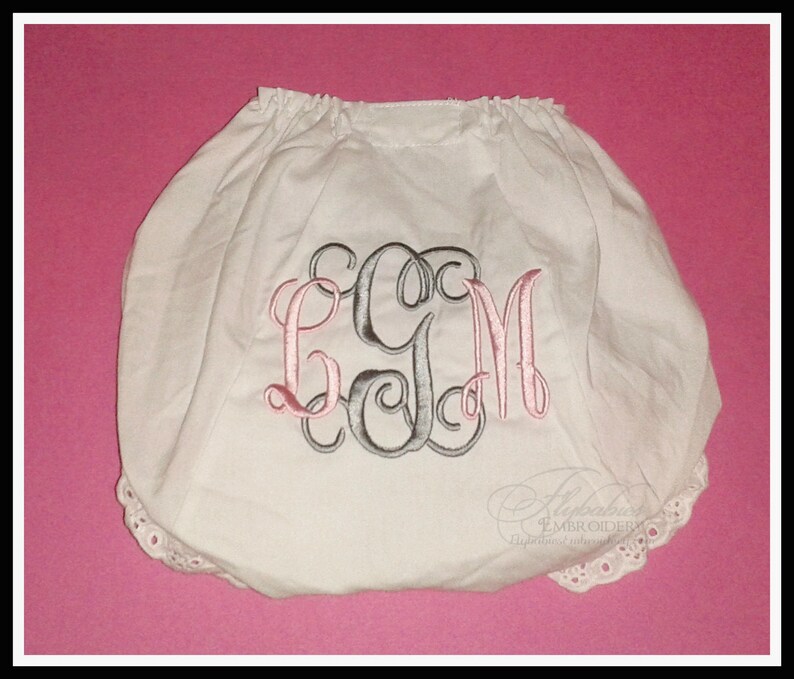 May include: White cotton baby bloomers with a pink and grey monogram "LGM" embroidered on the front. The bloomers have a white lace trim around the edges.