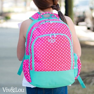 May include: A pink and teal polka dot backpack with a zippered front pocket and a monogrammed "NSR" on the front.
