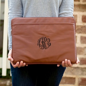 May include: A brown leather laptop sleeve with a monogrammed design. The monogram is in black and features the letters "LRG" in a script font.