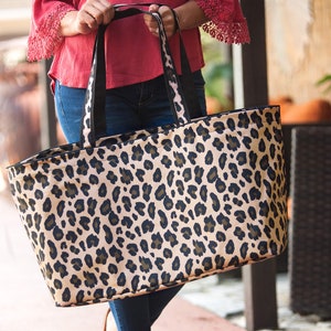 May include: A large tote bag with a leopard print design. The bag has black handles and a black trim around the top.