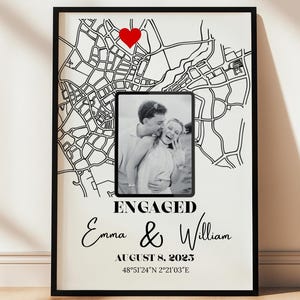 Puede incluir: Un marco negro con una impresión de mapa en blanco y negro, un corazón rojo y una foto en blanco y negro. La impresión dice "ENGAGED" con los nombres "Emma & William", la fecha "8 de agosto de 2023" y coordenadas.