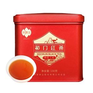 May include: A rectangular red metal tea tin featuring gold text and graphics, including the words Keemun Black Tea and a net weight of 100 grams. A small white ceramic cup filled with amber-coloured tea is positioned in front of the tin.