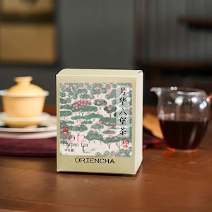 May include: A rectangular box of Oriencha Liu Pao Tea. The box has a green and pink floral design with Chinese characters and the text "2012 Liu Pao Tea". A yellow tea cup and a glass teapot with tea are in the background.