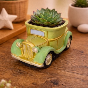 May include: A novelty planter in the shape of a classic car, painted in green and gold. The car planter contains a green succulent plant. The planter has detailed features such as headlights and a radiator grille.