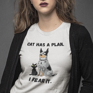 May include: White t-shirt with the text "CAT HAS A PLAN. I FEAR IT." featuring a cartoon dog and black cat. The dog is spotted with black markings. The cat is solid black.