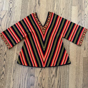 May include: A colorful, striped knit top with a V-neck. The top features a pattern of red, orange, and yellow stripes against a black background. The sleeves and neckline are trimmed with decorative patterns.