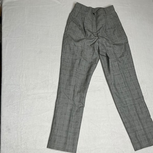 May include: Gray plaid trousers with a button closure and pleats. The pants are made of a woven fabric and have a classic, tailored design. The trousers are laid flat on a white surface.
