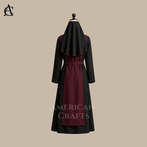 May include: A black and burgundy robe with a matching head covering. The long-sleeved garment features a burgundy panel down the front and a burgundy belt. The text "AMERICAN CRAFTS" is printed on the lower portion of the robe.