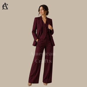 Op de afbeelding: Een diepbordeauxrood driedelig pak bestaande uit een getailleerde blazer met revers, een vest met knopen en een wijde broek met een vouw in het midden. Het ensemble heeft een consistente effen kleur over alle drie de bijpassende kledingstukken.