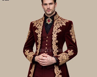 May include: A burgundy velvet suit with gold embroidery. The suit includes a long coat, waistcoat, and dress shirt. A red jeweled brooch accents the black dress shirt. The suit is formal wear.