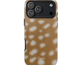 May include: A phone case with a brown and white spotted pattern, resembling deer fur. The case has a camera cutout with three lenses and the word "Canela" in cursive script at the bottom.