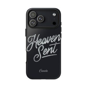 以下が含まれることがあります： 黒い携帯電話ケース。筆記体で「Heaven Sent」の文字が書かれています。ケースは光沢仕上げで、3つのレンズを備えたカメラモジュールが付いています。「Canela」という名前が下部に印刷されています。
