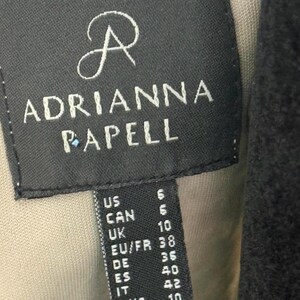 Pode incluir: Uma etiqueta preta com o nome da marca "ADRIANNA PAPELL" em letras brancas. Inclui convers&otilde;es de tamanhos para os tamanhos US, CAN, UK, EU/FR, DE, ES e IT. A etiqueta est&aacute; costurada numa pe&ccedil;a de vestu&aacute;rio.
