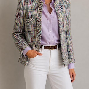 May include: A multi-colored tweed blazer with a woven grid pattern, featuring white piping along the edges and two front pockets. It is worn over a light purple button-down shirt, a brown leather belt with a gold buckle, and white denim jeans.