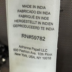 Pode incluir: Close-up de uma etiqueta de tecido branco com texto em v&aacute;rios idiomas: Made in India, Fabricado en Inda, Fabriqu&eacute; en Inde, Hergestellt in Indien, Geproduceerd te India. A etiqueta tamb&eacute;m inclui o texto RN#59782 e Adrianna Papell LLC, 500 Fashion Ave., New York, USA, NY 10018.